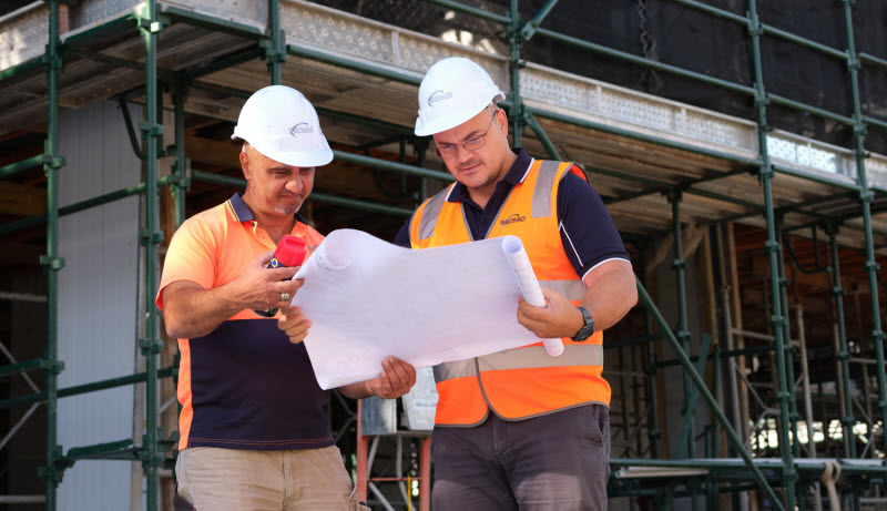 Two engineers wearing hard hats and uniform checking the plan at the construction site