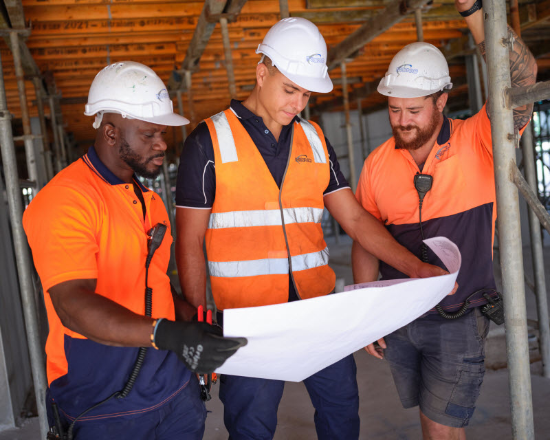 Three men wearing safety vest in the field checking the blueprint of the construction site