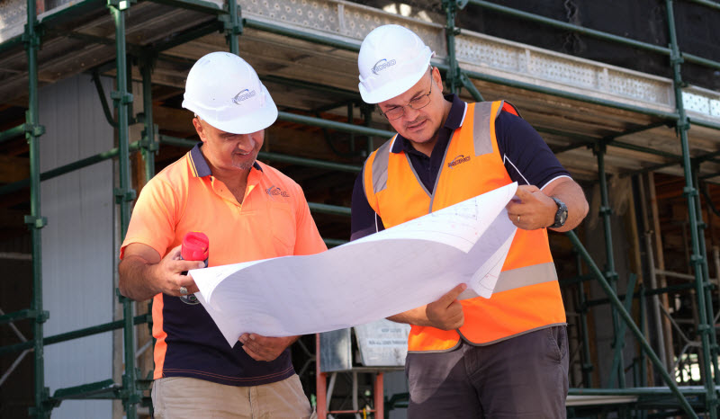 Two men wearing hard hats checking the floor plan at the construction site